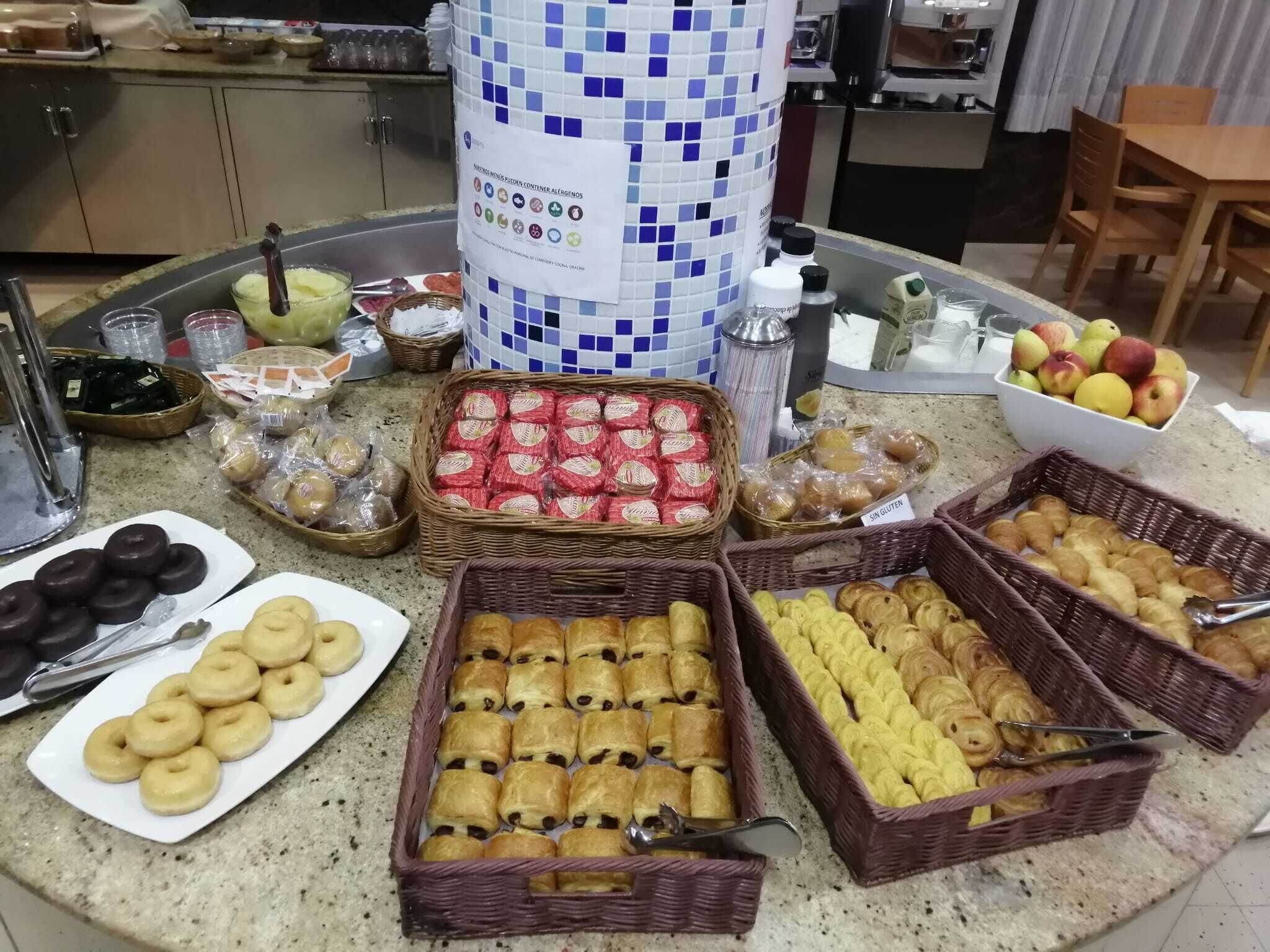 Una mesa de buffet con diversos alimentos, entre ellos pasteles, frutas y salsas.