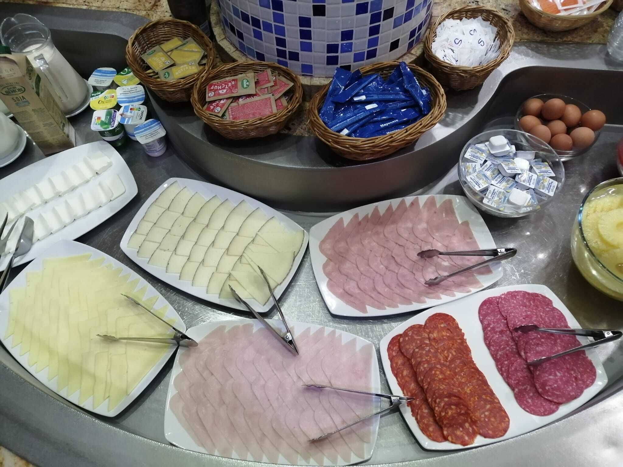 A buffet table with various food items including sliced meats, cheeses, and condiments.