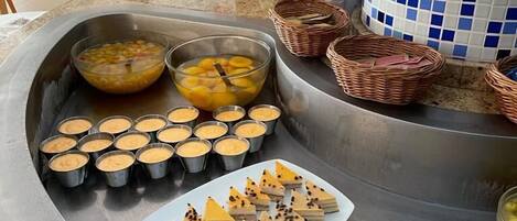 A buffet with various dishes including custard cups, a plate of layered desserts, and a dish with shredded cheese and meat.