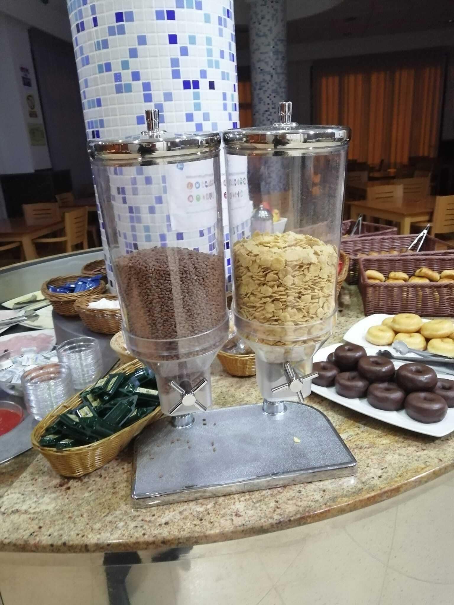 Un montaje tipo buffet con recipientes transparentes de granola y trozos de chocolate, un plato de rosquillas de chocolate y cestas de pasteles.