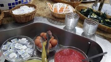Montaje de bufé con diversas opciones de comida, incluyendo pan, pasteles y un bol de frutas con trozos de piña.