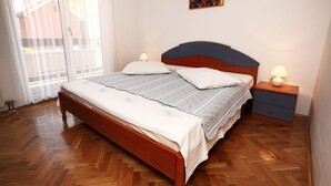 A bedroom with a wooden bed, two bedside tables with lamps, a window with sheer curtains, and a small decorative item on the wall. - Apartments Adriatic (Podstrana)