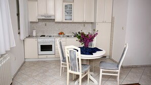A modern kitchen with white cabinets, a stove, and a dining table with chairs. - Apartments Adriatic (Podstrana)