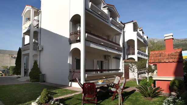 A two-story building with balconies, a small garden, and outdoor seating. - Apartments Adriatic (Podstrana)