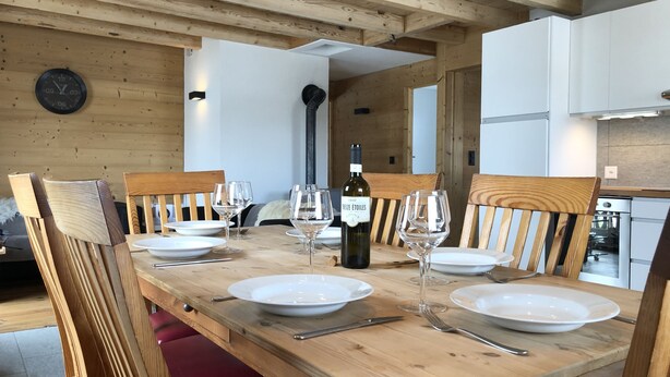 A wooden dining table set with plates, wine glasses, and cutlery, surrounded by wooden chairs. - Chalet - La Tzoumaz (La Tzoumaz)