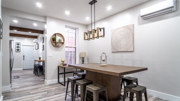 A modern kitchen with a central island, bar stools, pendant lighting, and a view to the dining area.