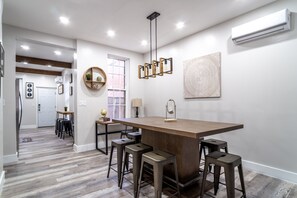 Una cocina moderna con una isla central, taburetes de bar, iluminación colgante y vistas al comedor.