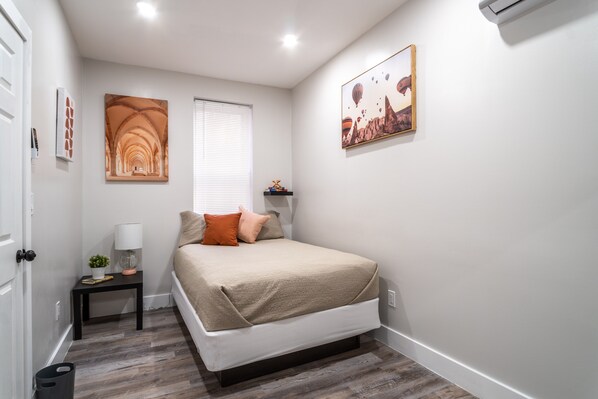 A bedroom with a bed, a nightstand, a window, and wall art.