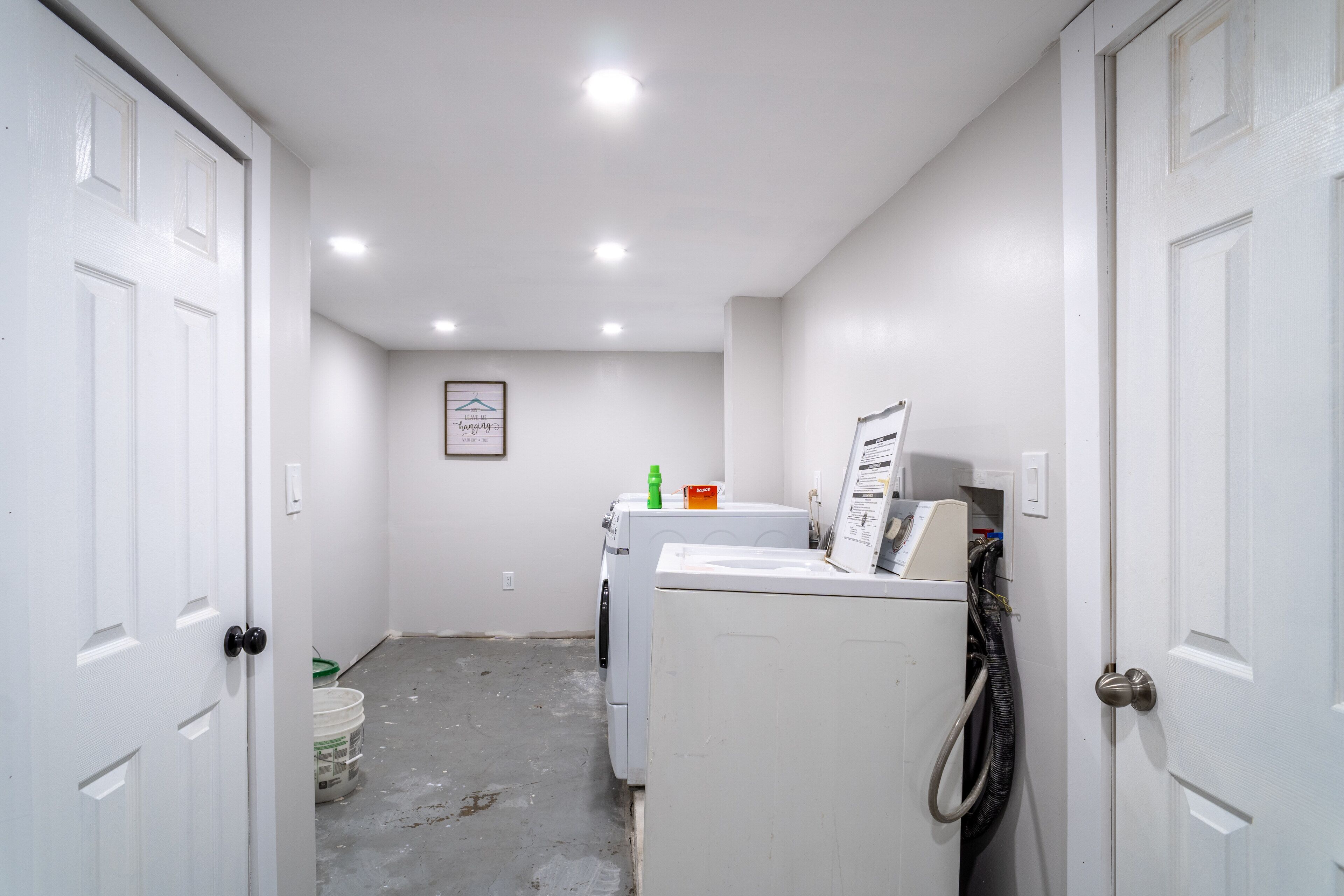 A laundry room with a washing machine and dryer, a framed sign on the wall, and a door on the left.