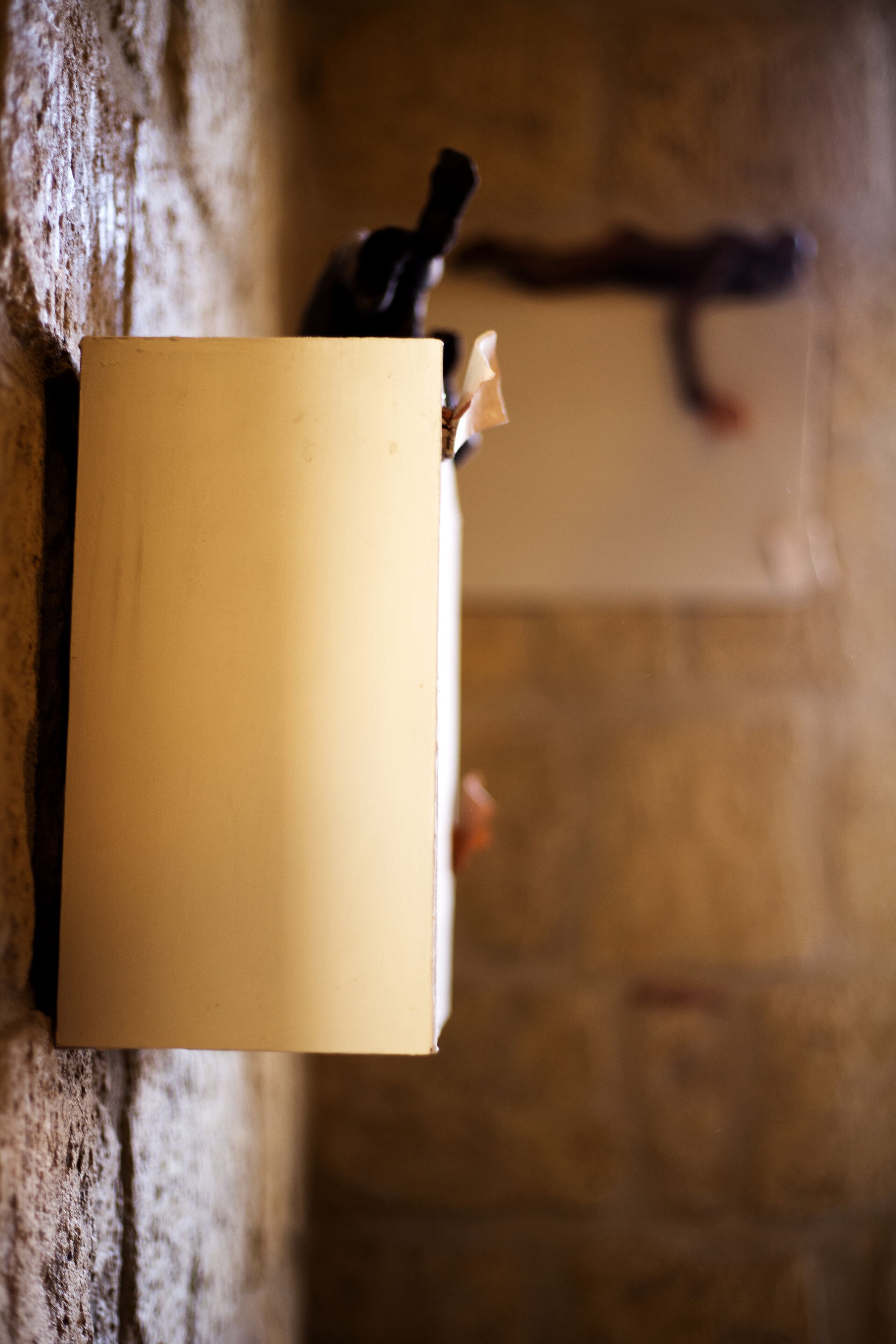 A wall-mounted book with a pen and a small object, possibly a candle, on a textured wall.