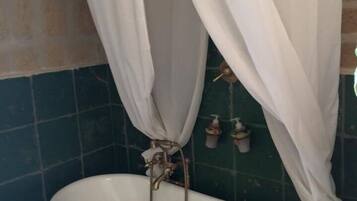 A bathtub with a shower head, a curtain, and a wall-mounted soap dispenser.