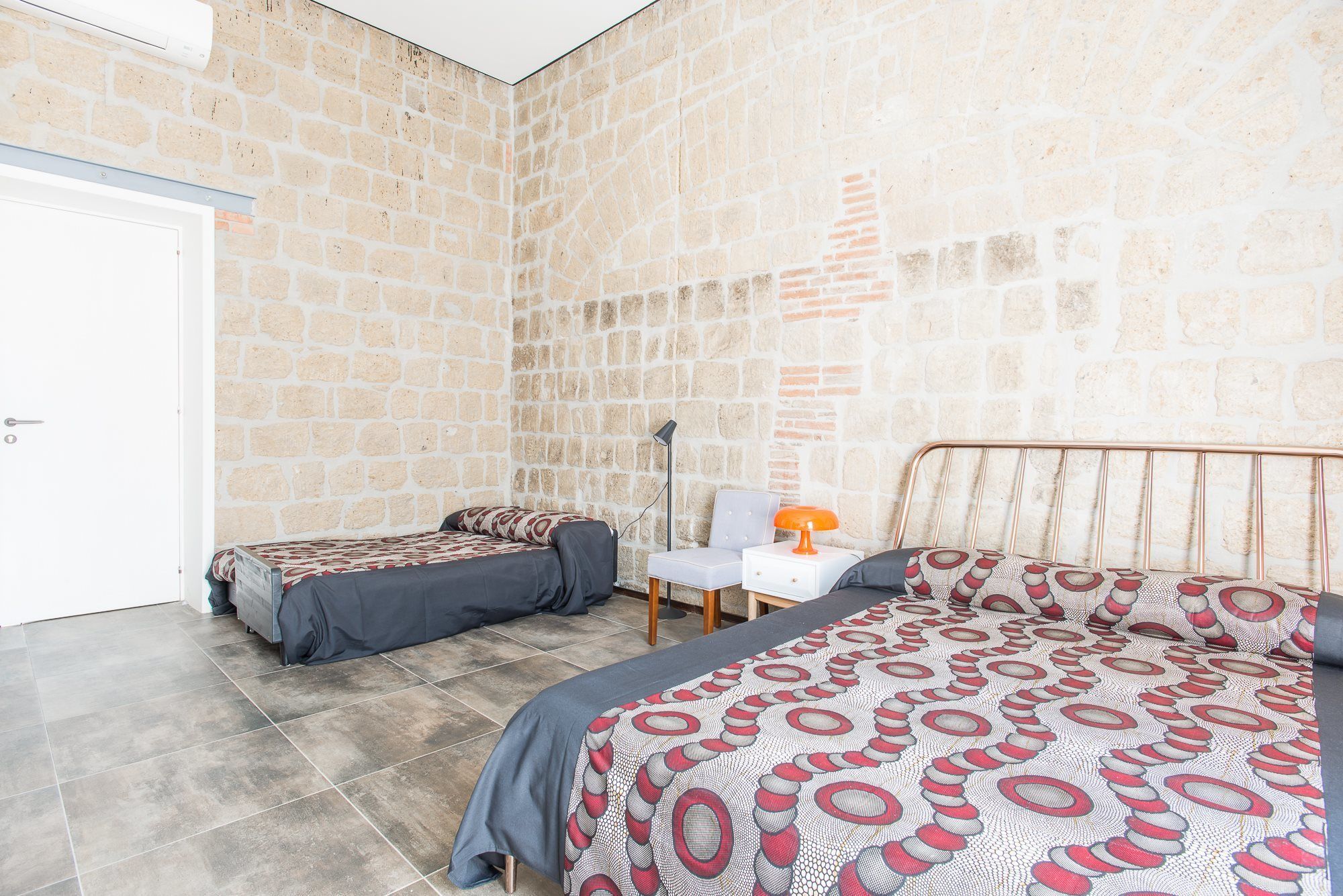 Ein Zimmer mit zwei Betten, einem Sessel, einer Lampe und einer weißen Tür.