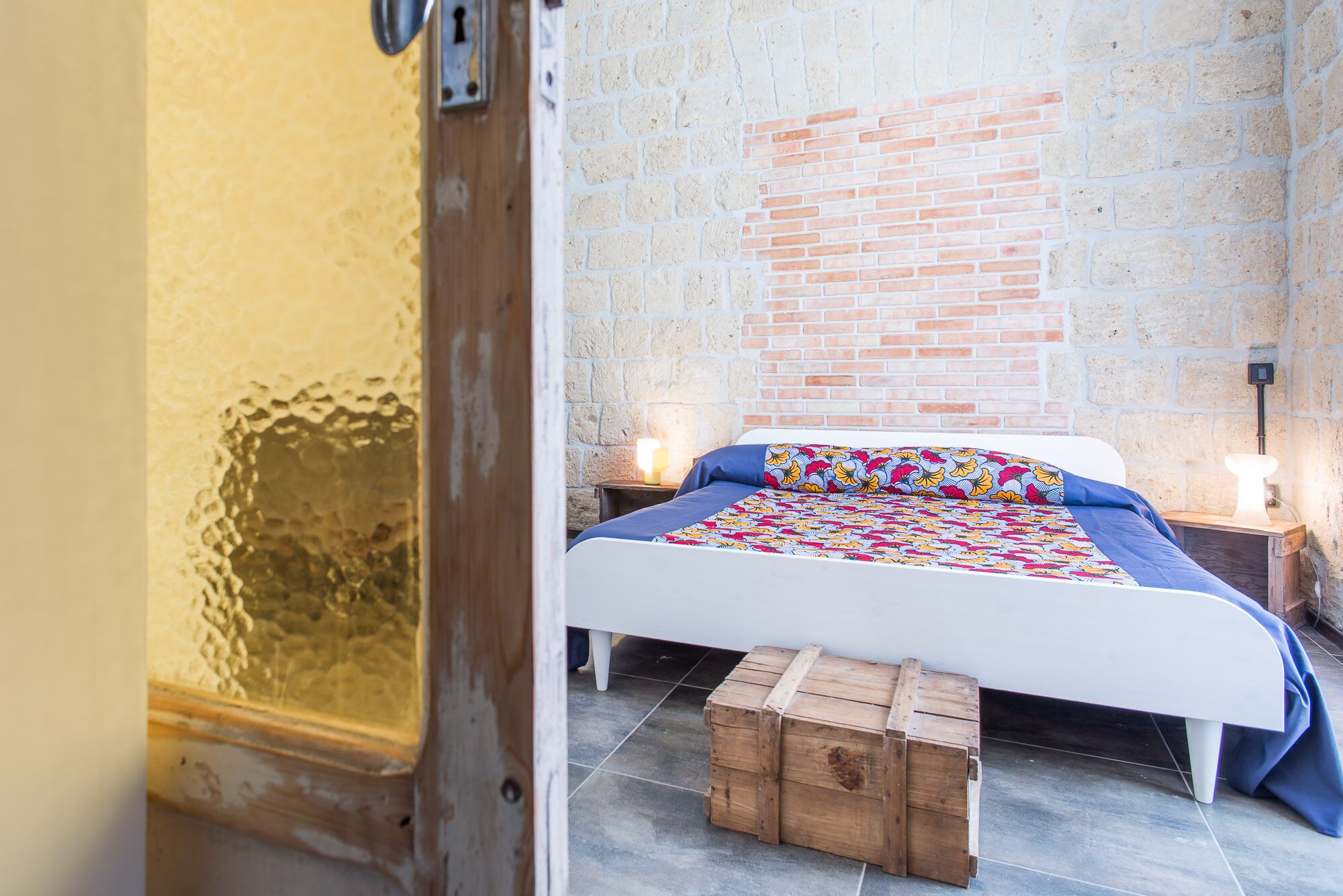 Une chambre à coucher avec un lit, des tables de chevet en bois, un mur en briques et une porte.