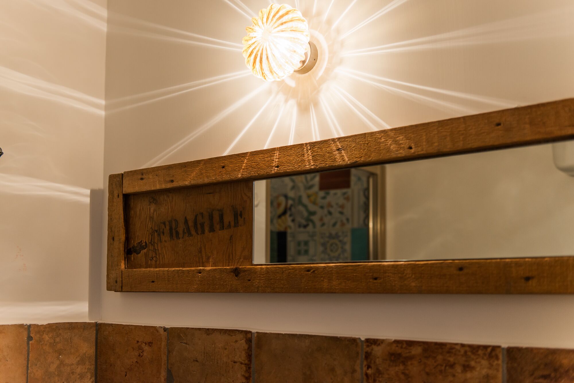 Un miroir à cadre en bois, avec un luminaire placé au-dessus.