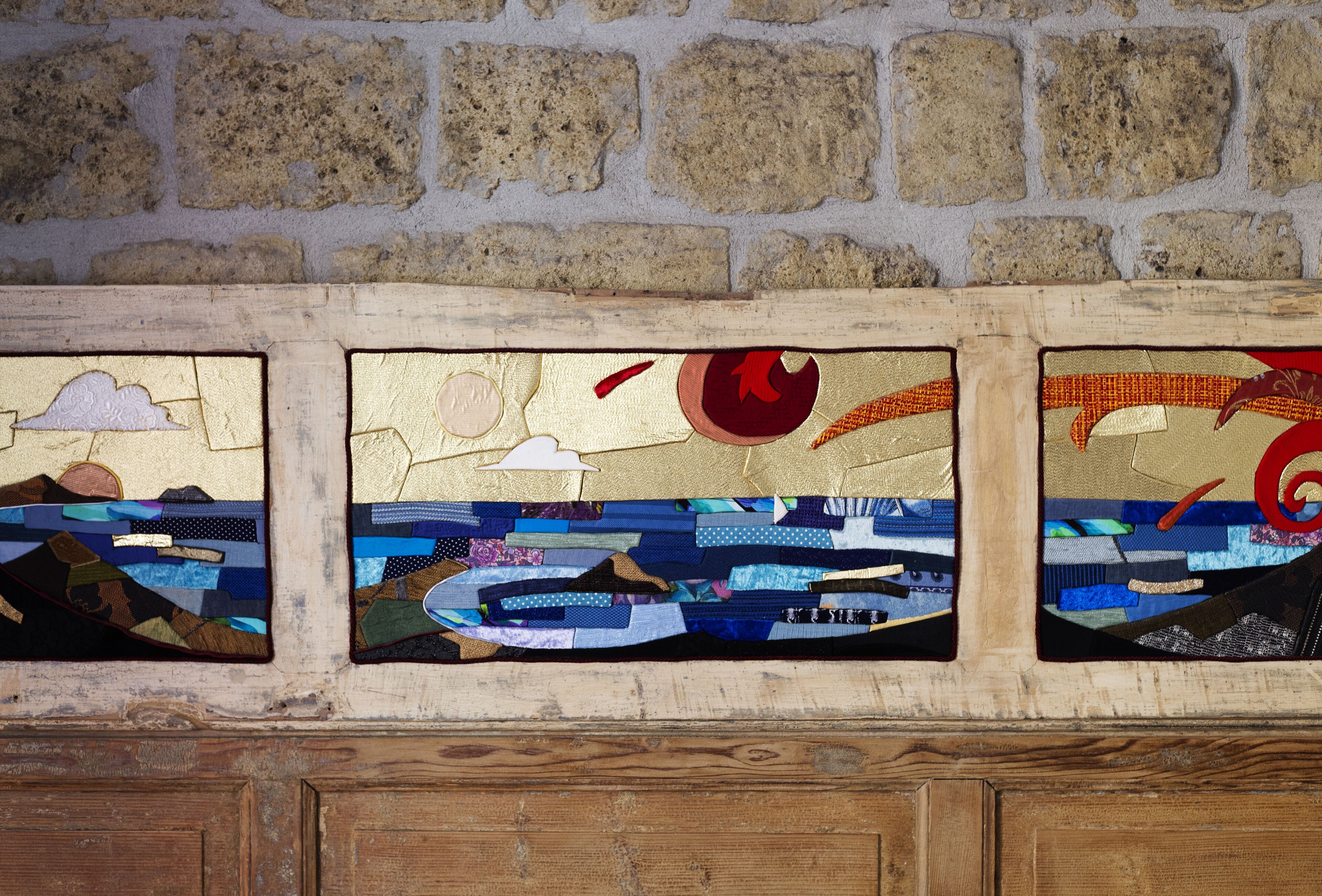 A wall with three stained glass panels depicting scenes with clouds, a sun, and a red spiral.