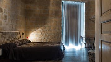 A bedroom with a stone wall, a bed, a chair, and a window with curtains.