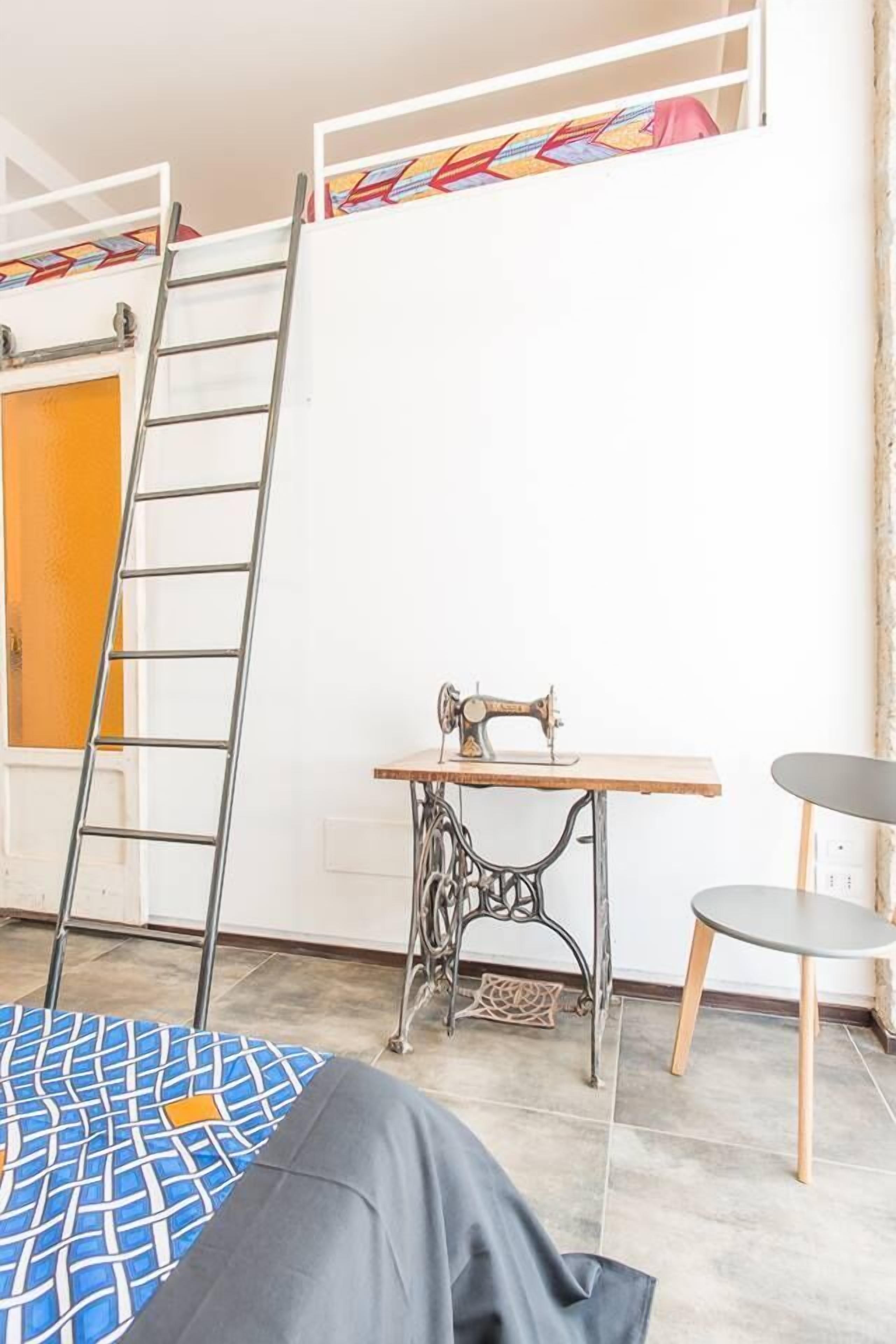 Quarto com cama beliche, máquina de costura, escada, mesa pequena e cadeira.
