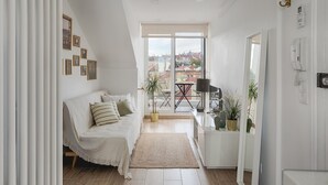 A modern living room with a sofa, a small table, and a view of the city through large windows. - Romantic Gem in Alcântara (Lisboa)