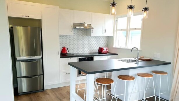 Una cucina moderna con mobili bianchi, un frigorifero in acciaio inossidabile, un piano di lavoro nero e una zona bar con sgabelli.
