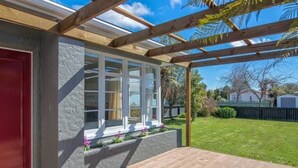 Un'area patio coperta con una pergola in legno, una porta rossa e una finestra con stipiti bianchi.