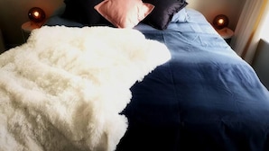 Un letto rifatto con un copriletto blu e una coperta bianca e soffice, arricchito da diversi cuscini in diverse tonalità.