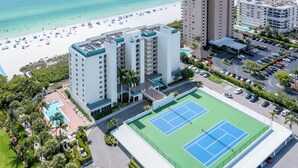 An aerial view of a hotel with a tennis court, pool, and beach access.