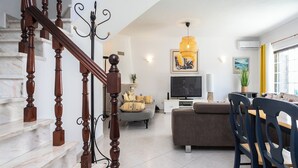 Un salon moderne avec un escalier, un téléviseur à écran plat, un canapé et un coin repas.