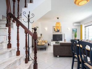 Un salon moderne avec un escalier, un téléviseur à écran plat, un canapé et un coin repas.