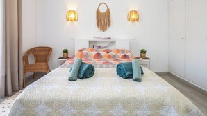 Une chambre à coucher comprenant un lit, deux lampes fixées au mur, un fauteuil en osier et une plante fixée au mur.