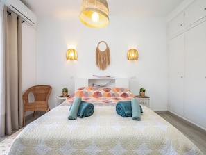 Une chambre à coucher comprenant un lit, deux lampes fixées au mur, un fauteuil en osier et une plante fixée au mur.