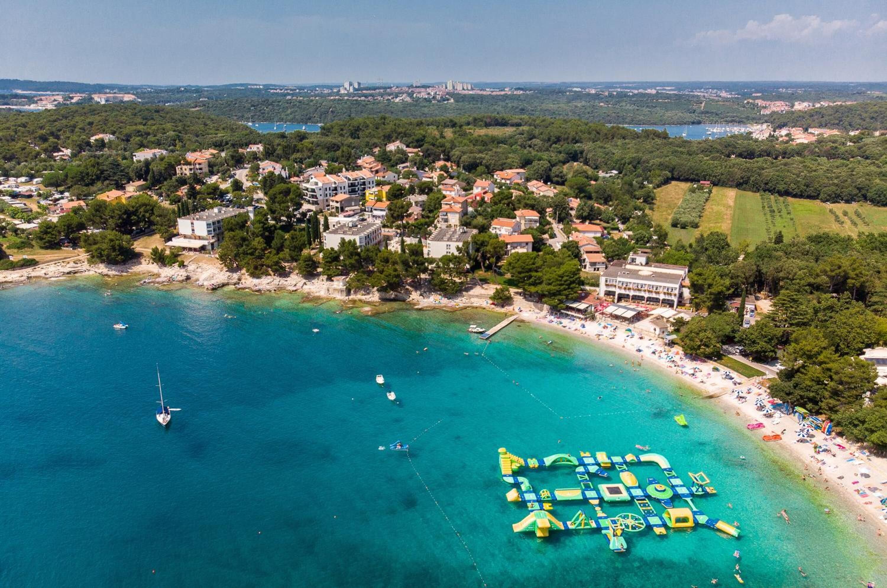 Vue aérienne d’une ville côtière avec une plage, des bateaux et un port de plaisance.