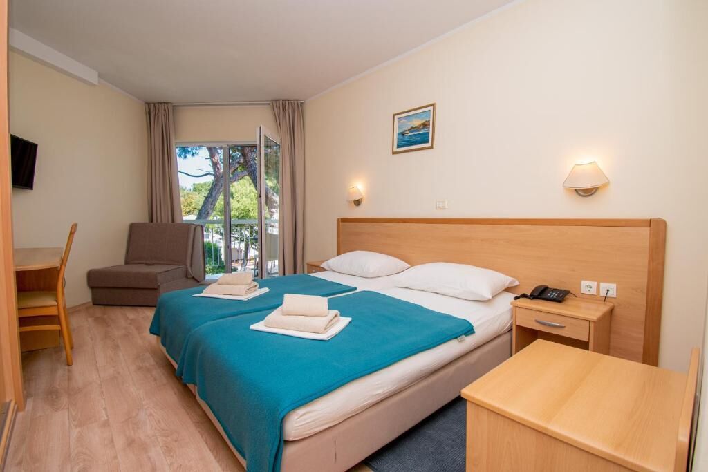 Une chambre d’hôtel avec un lit, un bureau, une chaise, une table de chevet et une fenêtre avec des rideaux.