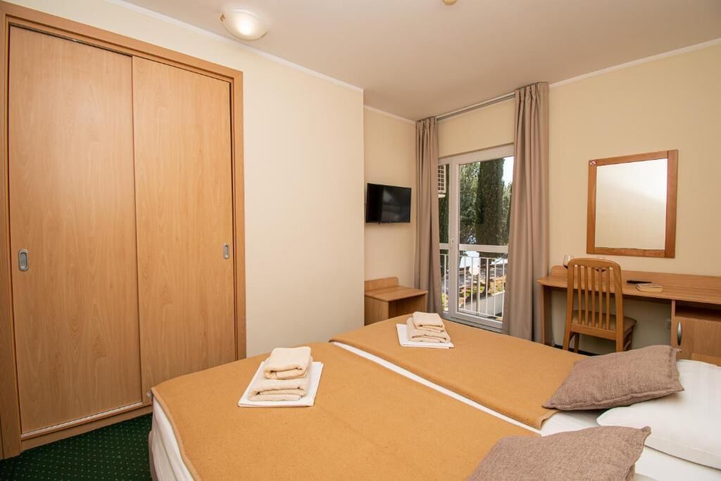 Une chambre d’hôtel avec deux lits, une télévision, un bureau, une chaise et une grande fenêtre.