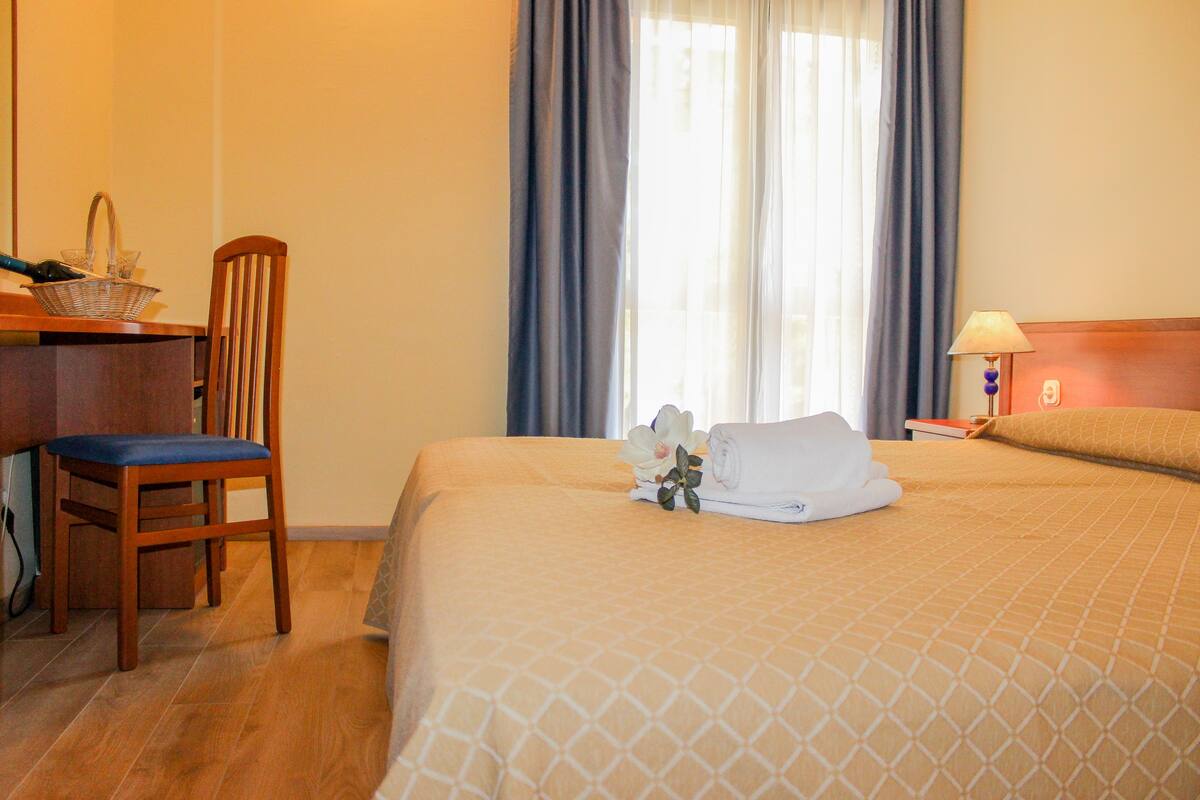Habitación de hotel con cama, escritorio, silla, lámpara y ventana con cortinas.