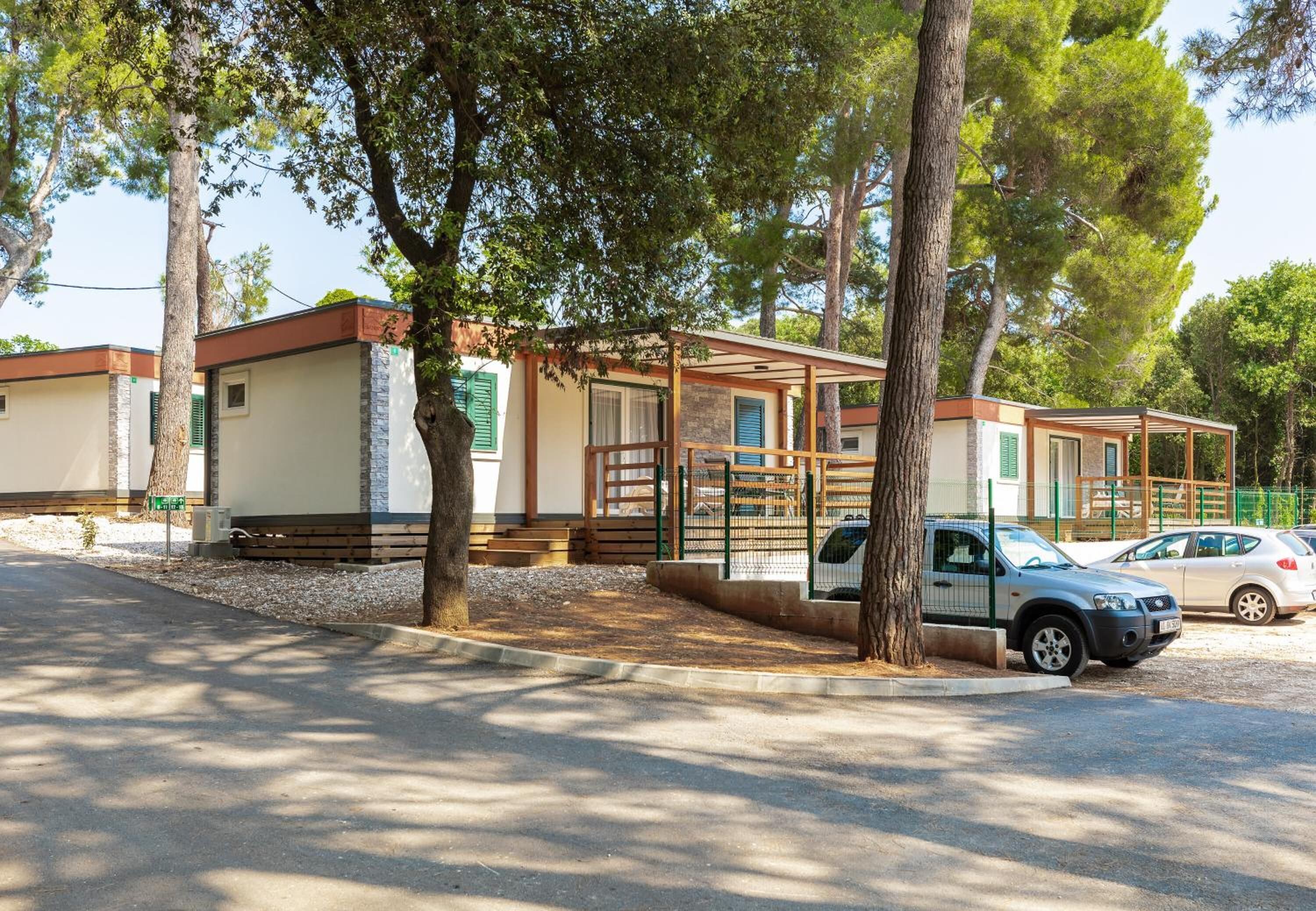 A row of mobile homes with a covered parking area and a tree-lined street.