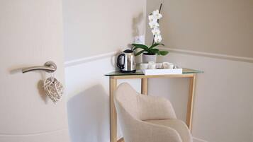 A room with a white door, a glass table with a kettle and a potted plant, and a beige chair.