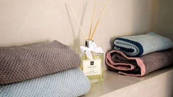 A shelf with a bottle of essential oil, reed diffusers, and folded towels in various colors.