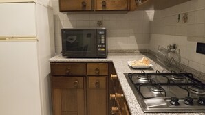 A kitchen with wooden cabinets, a microwave, a gas stove, and a plate of food on the counter. - Casa Bella Riva Reno - In the Heart of Bologna (Bologna)