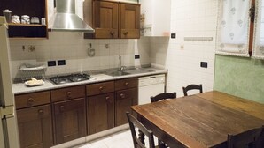 A kitchen with wooden cabinets, a stainless steel range hood, a dishwasher, and a wooden dining table with chairs. - Casa Bella Riva Reno - In the Heart of Bologna (Bologna)