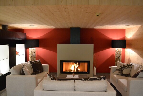 A cozy living room with a fireplace, two white sofas, and red walls. - Hotel Regglbergerhof (Nova Ponente)