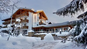 A multi-story hotel with wooden balconies and a stone facade, surrounded by snow-covered trees and a clear sky. - Hotel Regglbergerhof (Nova Ponente)