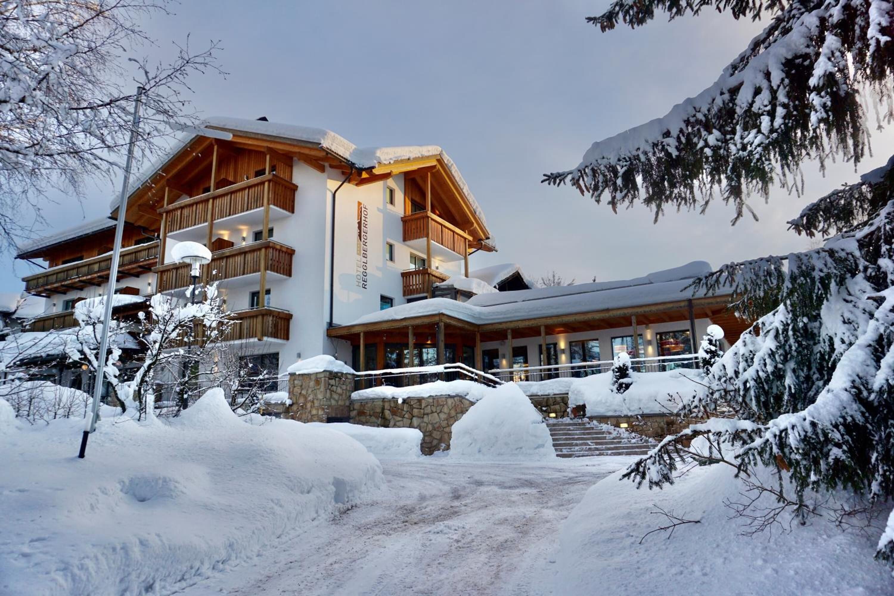 Un hotel de varios pisos con balcones de madera y fachada de piedra, rodeado de árboles cubiertos de nieve y un cielo despejado.