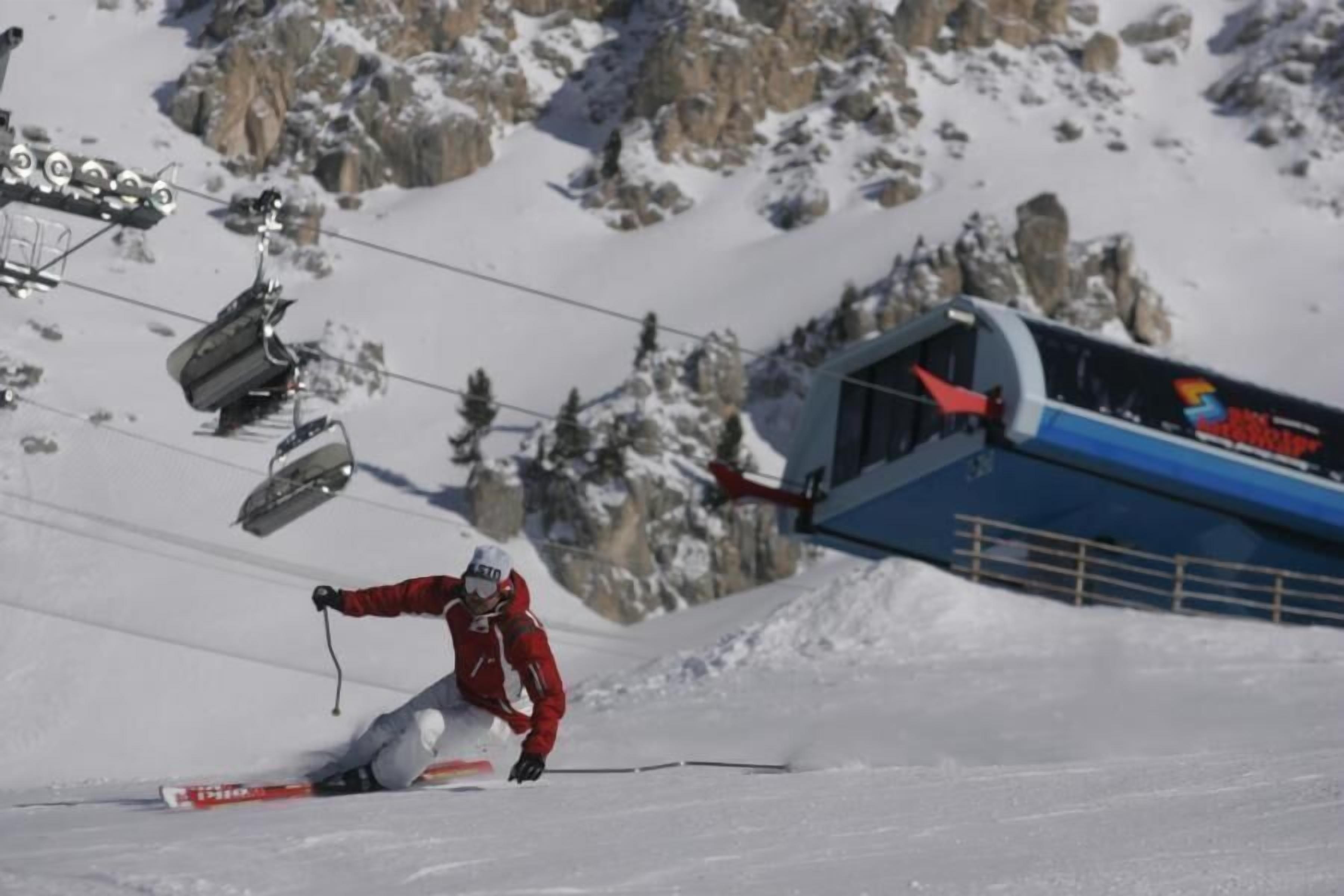 A ski slope with a skier in motion, a ski lift in the background, and a mountain landscape.