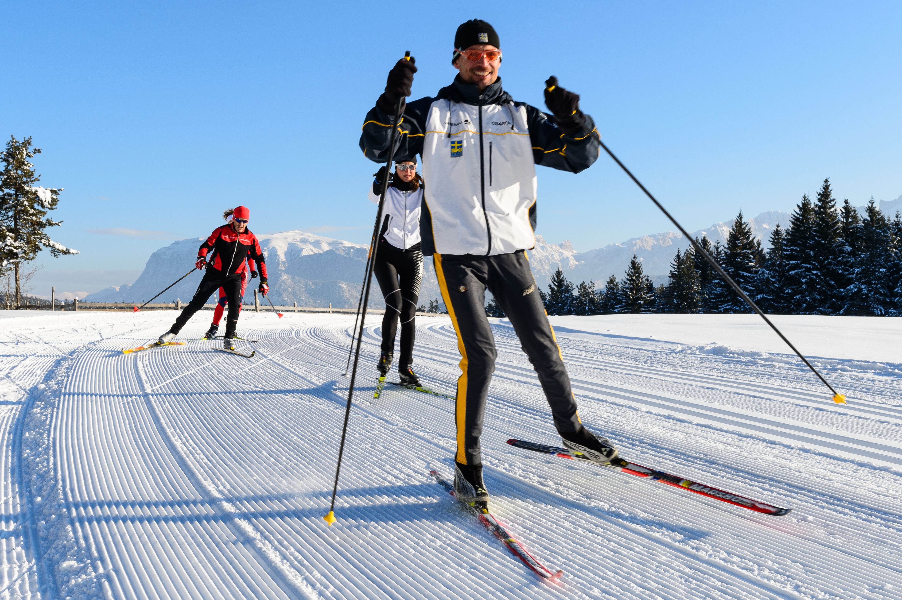 Trois skieurs sur une pente enneigée, avec des montagnes en arrière-plan.