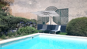A swimming pool with two lounge chairs and a large umbrella.