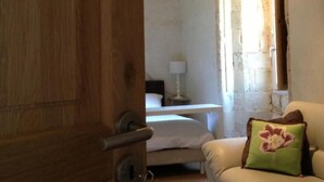 A bedroom with a wooden door, a bed, a nightstand, a lamp, and a sofa with a pillow.