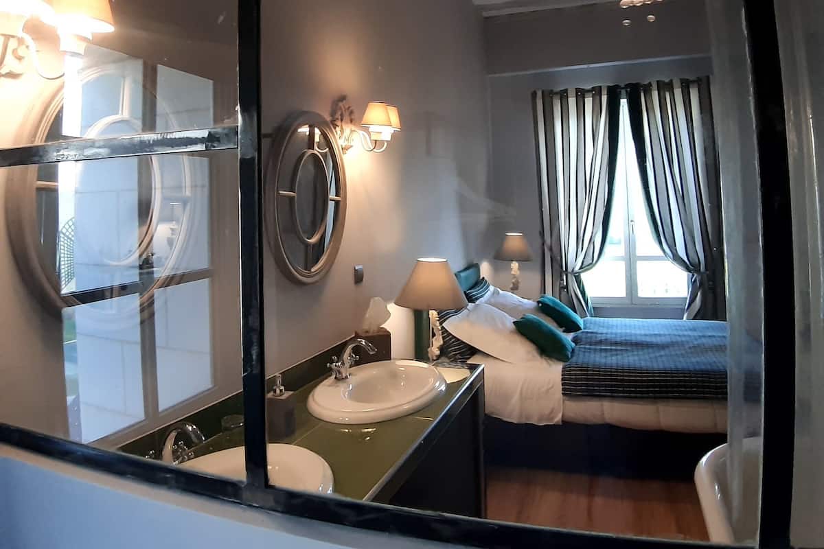 Ein Hotelzimmer mit großem Spiegel, einem Bett mit Kopfteil, einem Nachttisch mit Lampe, einem Fenster mit Vorhängen und einer Kristallleuchter.