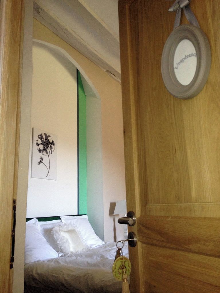 Una habitación de hotel con una cama, una pared verde, una obra de arte floral enmarco y una puerta de madera con un espejo y un llavero.