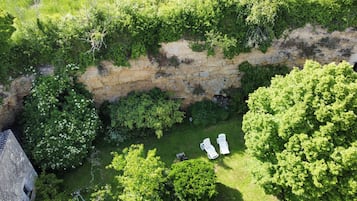 Vista aérea de um jardim com muro de pedra, vegetação exuberante e duas cadeiras de descanso brancas.