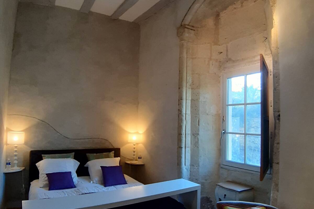 Ein Schlafzimmer mit Bett, Nachttischlampen, einem Fenster und einem Sessel.